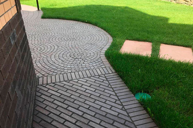 Curved herringbone paved path alongside a green lawn