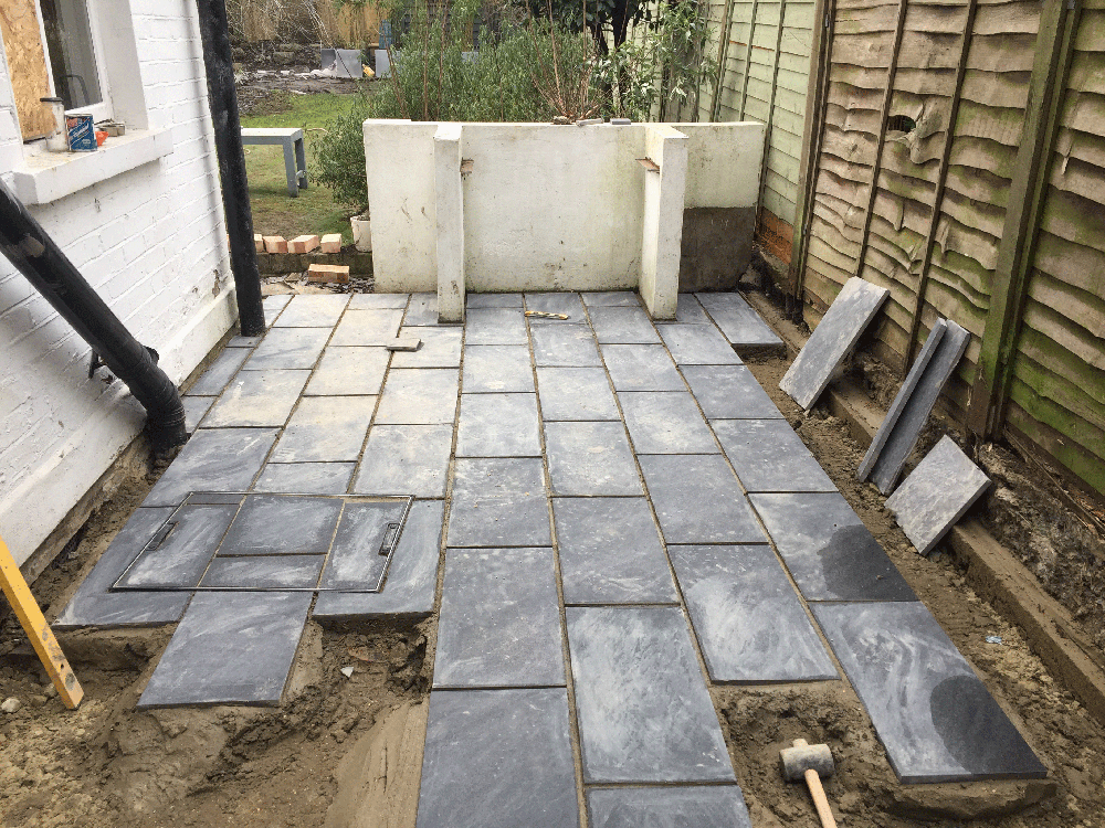 Grey stone paving slabs being laid around the patio